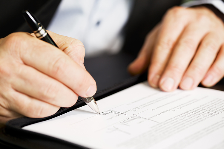 Businessman sitting at office desk signing a contract with shallow focus on signature.